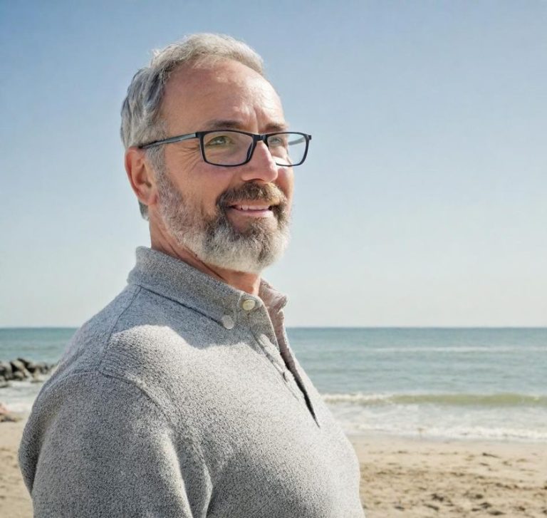 Junger Mann mit braunem Haar, lächelnd in einem blauen Hemd, steht an einer Wand.